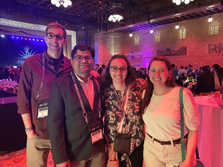 Four people smiling under colorful lights
