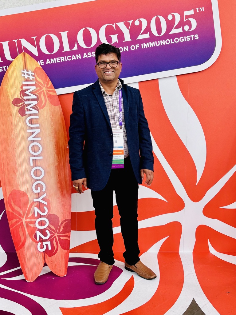 Shailesh standing next to a conference sign and a surf board