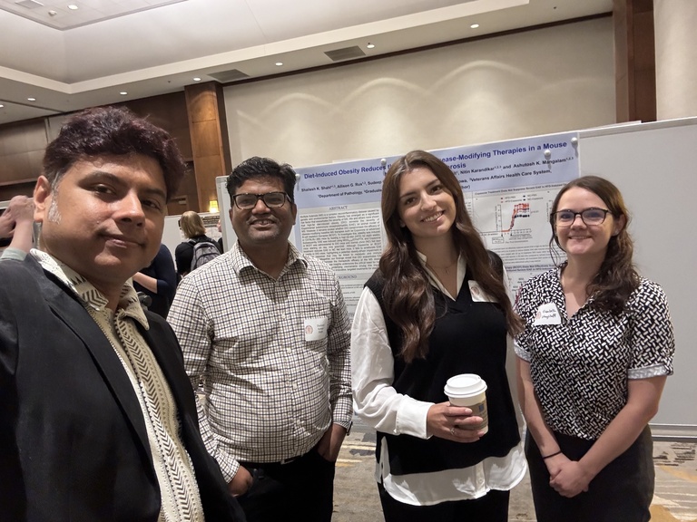 Four people smiling in front of a research poster